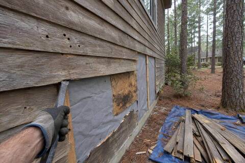 Weathered cedar lap siding being pried off a wall, with house wrap underneath