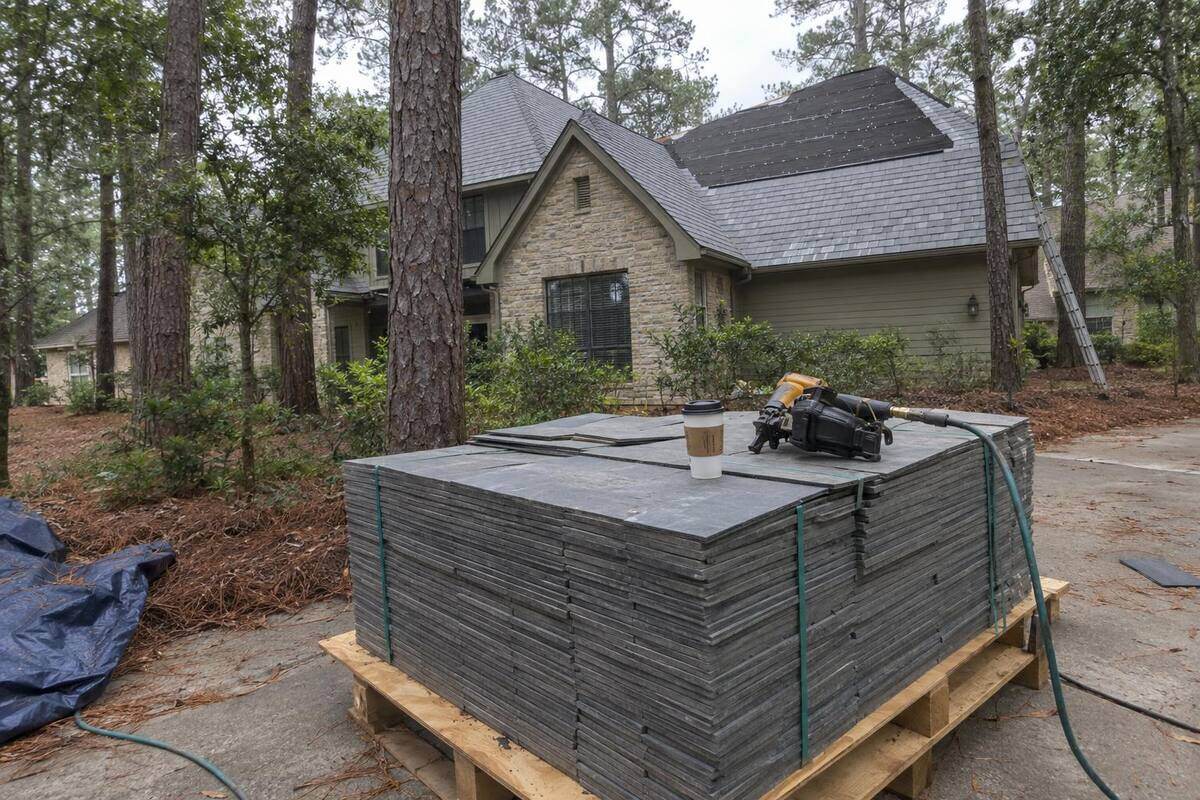 Gray fiber-cement roofing slates stacked on a pallet beside a partly finished roof